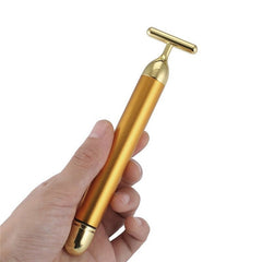 Hand holding a 24k gold facial roller with a T-shaped massaging head for skincare